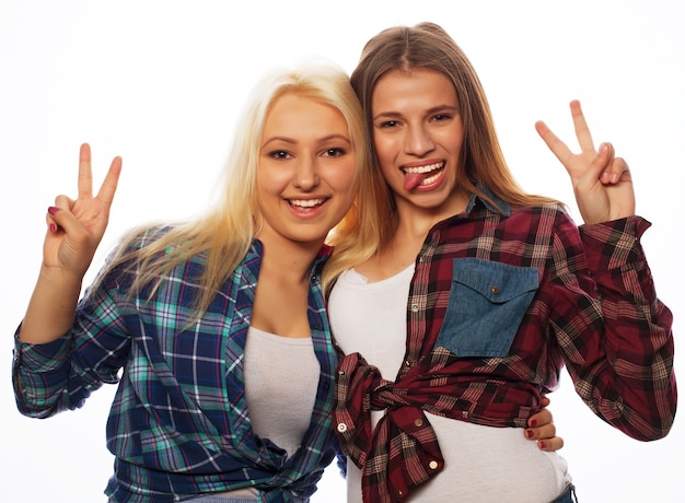 Zdjęcie dwie młode dziewczyny stojące razem i zabawy. pokazywanie znaków rękami. patrząc w kamerę