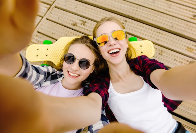 Dwie młode dziewczyny w stroju hipster co selfie leżąc na drewnianym molo.