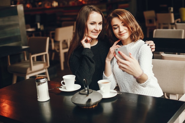 dwie młode i piękne dziewczyny siedzą w kawiarni i piją kawę