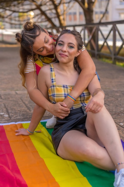 Dwie młode kaukaskie przytulające się kobiety z flagą dumy LGBT na zewnątrz