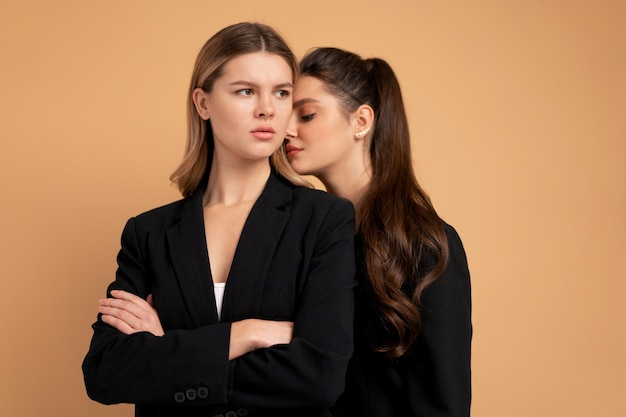 Dwie młode kobiety biznesu ubrane w czarny garnitur stojący studio pomarańczowy kolor tła