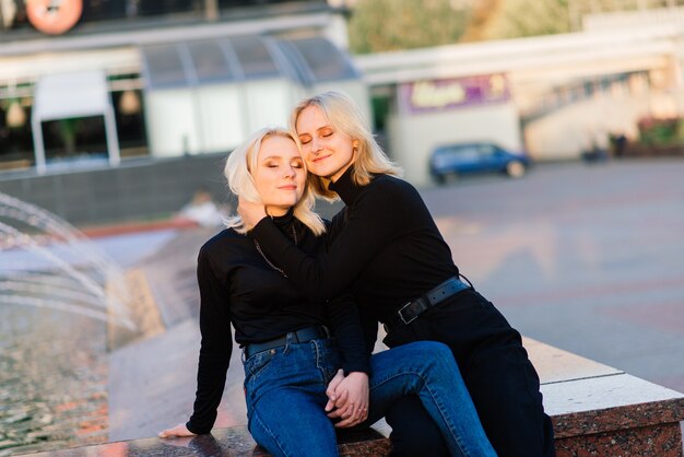 Dwie młode kobiety chodzą uśmiechnięte obejmując się i całując na świeżym powietrzu w mieście