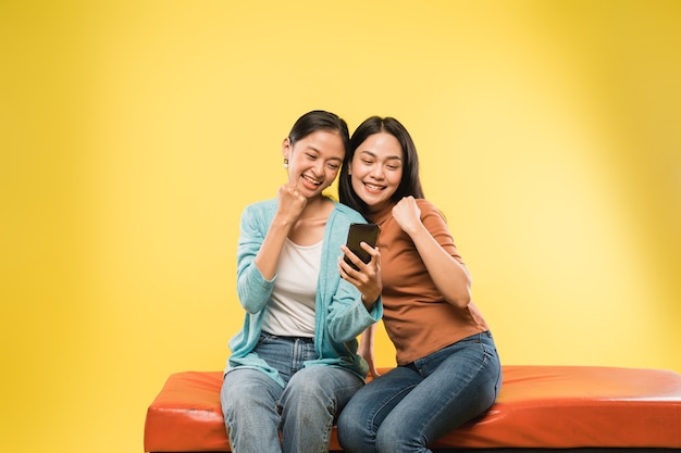 Dwie młode kobiety szczęśliwe z zaciśniętymi rękami, patrząc na ekran telefonu komórkowego