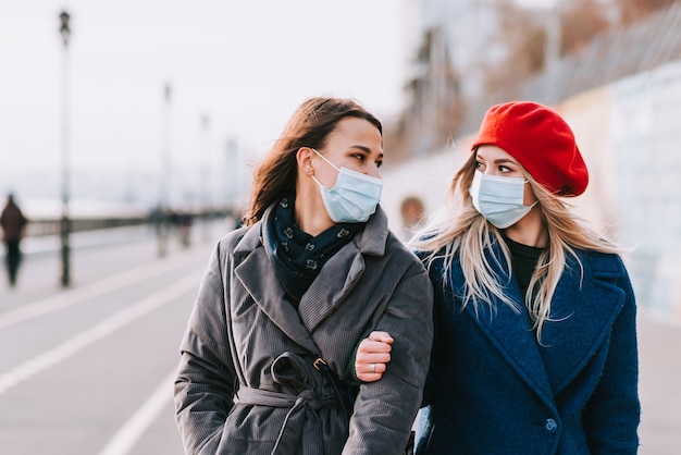 Dwie młode kobiety w maskach medycznych idą razem ulicą