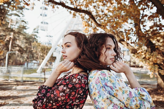 Dwie młode kobiety w sukienkach vintage stoją w jesiennym parku, obejmując się