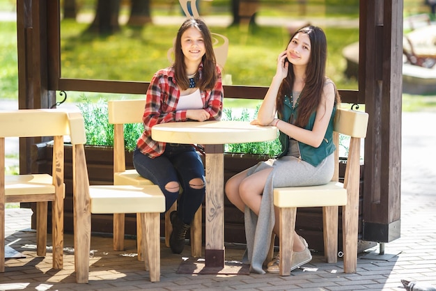 Dwie młode koleżanki siedzą i rozmawiają przy stole w miejskiej kawiarni