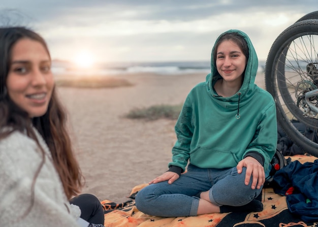 Dwie młode latynoski uśmiechnięte patrząc na kamerę siedzącą na plaży