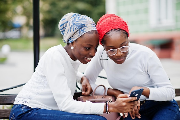Dwie młode, nowoczesne, modne, atrakcyjne, wysokie i szczupłe afrykańskie kobiety muzułmańskie w chuście na głowę hidżab lub turban pozowane razem z telefonami komórkowymi pod ręką