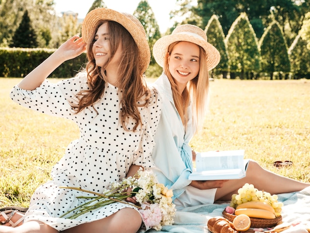 Dwie młode piękne hipster kobieta w modnej letniej sukience i kapeluszach. Beztroskie kobiety robią piknik na zewnątrz.