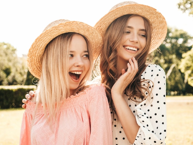 Dwie młode piękne uśmiechnięte hipster kobieta w modnej letniej sukience. Seksowne beztroskie kobiety pozują w parku w kapeluszach.