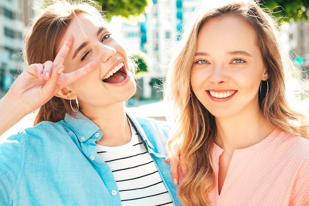 Zdjęcie dwie młode piękne uśmiechnięte kobiety hipster w modnych letnich ubraniach i sukienceseksowne beztroskie kobiety pozują na tle ulicy
