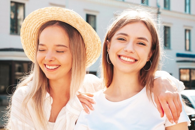 Dwie młode piękne uśmiechnięte kobiety hipster w modnych letnich ubraniachSeksowne beztroskie kobiety pozują na ulicy w kapeluszu Pozytywne czyste modele zabawy o zachodzie słońca