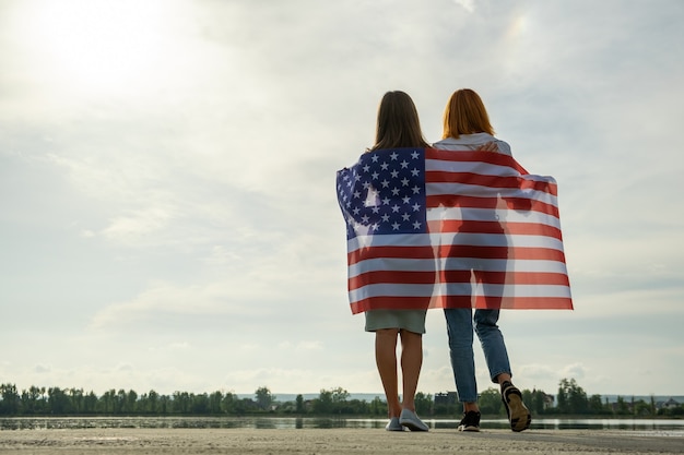 Dwie młode przyjaciółki stojące razem z narodową flagą USA na ramionach