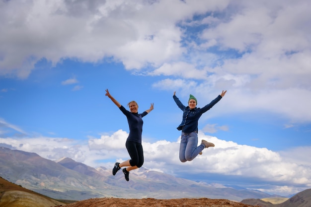 Dwie młode szczęśliwe dziewczyny skaczą unosząc ręce ze spektakularnym widokiem na góry.