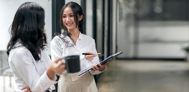 Dwie młode uśmiechnięte azjatyckie bizneswoman stojące w biurze dyskutują z nowym projektem startowym analizują planowanie i statystyki finansowe