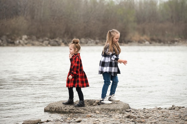 dwie młodsze siostry ubrane we wzorzyste ubrania w kratę bawią się bawiąc się nad rzeką