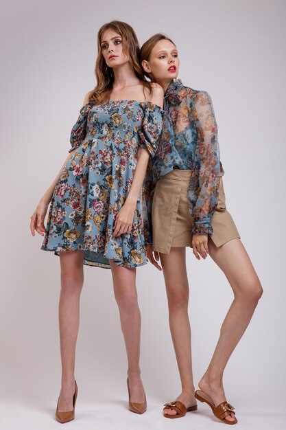 Dwie modne modelki w niebieskiej przezroczystej bluzce z kwiatowym wzorem ubierają beżowe szorty