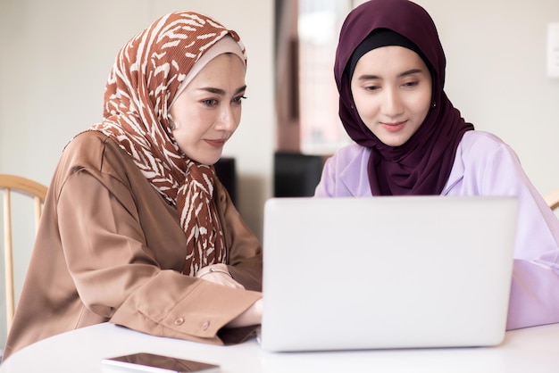 Dwie muzułmanki używające laptopa do wyjaśniania informacji biznesowych w pokoju