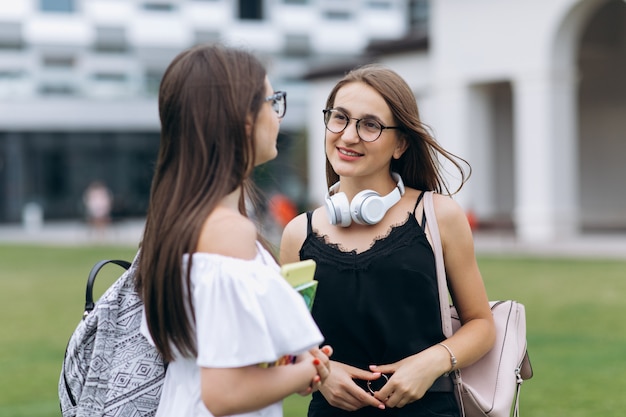 Dwie nastolatki rozmawiają razem w kampusie. Dwa żeńskiego studenta collegu podczas gdy stojący outdoors dużego miastowego budynek