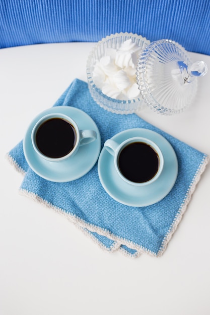 Dwie niebieskie filiżanki kawy na niebieskim serwetce i szklanym słoju z pianki