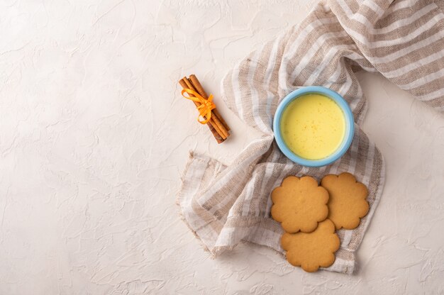 Dwie niebieskie filiżanki z tradycyjną indyjską herbatą masala chai, laskami cynamonu i ciasteczkami na lnianej serwetce