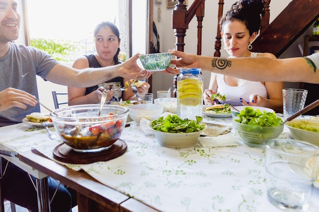 Dwie osoby jedzące lunch z przyjaciółmi podają miskę z jedzeniem na stole, ciesząc się i jedząc razem