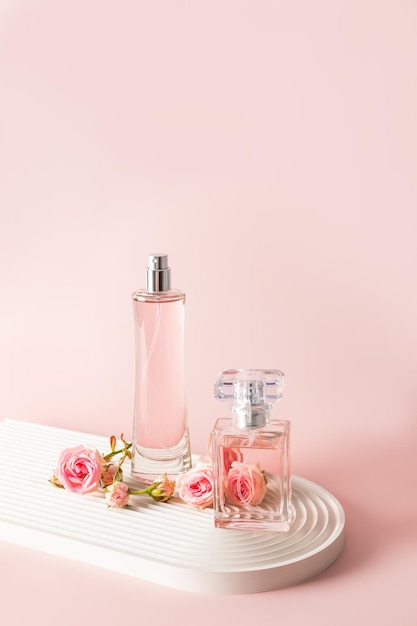Dwie piękne butelki kobiecych perfum lub wody perfumowanej na białym podium z małymi różowymi różami Widok pionowy z przodu Miejsce na kopię