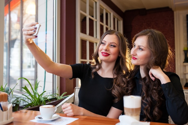 Dwie piękne dziewczyny robią selfi i piją kawę