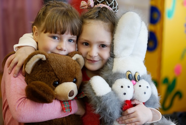 Dwie piękne dziewczyny z miękkimi zabawkami uśmiechają się do dzieci koleżanek w przedszkolu