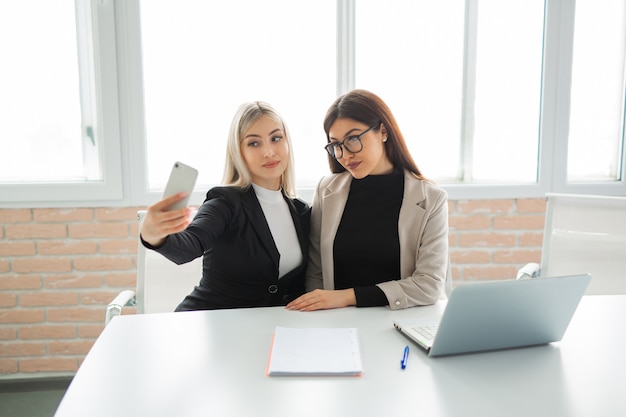 dwie piękne młode kobiety w biurze są fotografowane przez telefon