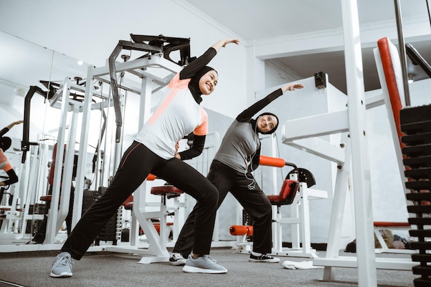 Dwie piękne muzułmańskie kobiety rozciągają się i ćwiczą razem w siłowni.
