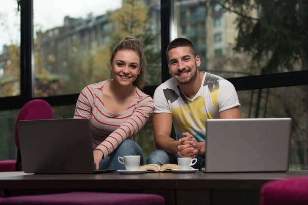 Dwie piękne studentki pijące i bawiące się laptopem w kafeterii