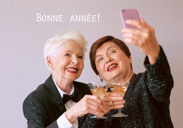 Zdjęcie dwie piękne, stylowe, dojrzałe starsze kobiety piją wino i robią selfie.