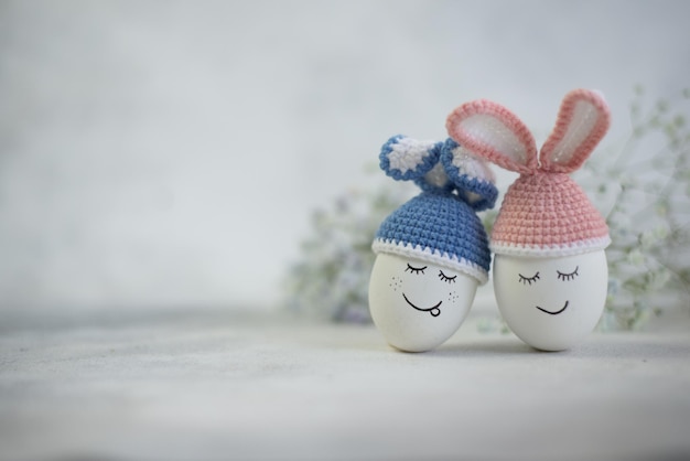 Dwie pisanki w uszach królika w niebiesko-różowych czapkach