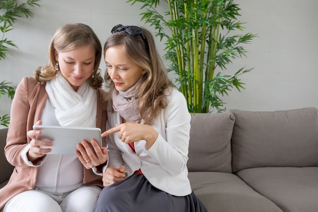 Dwie poważne kobiety za pomocą tabletu w salonie