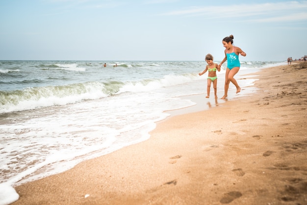 Dwie Pozytywne Dziewczynki Biegają Wzdłuż Piaszczystej Plaży W Słoneczny, Ciepły Letni Dzień