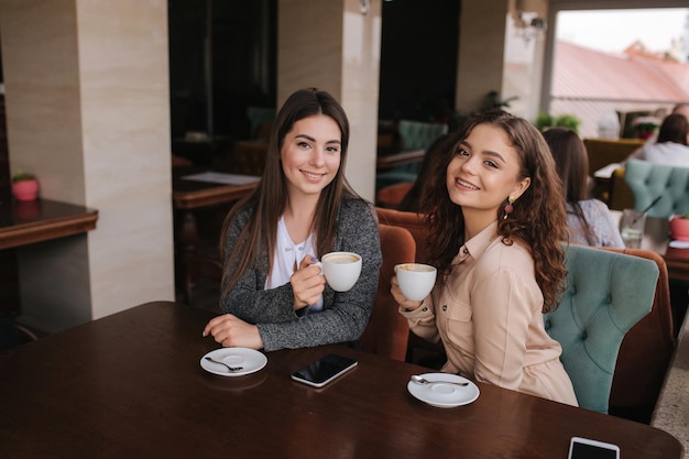 Dwie przyjaciółki piją kawę w restauracji i rozmawiają Piękne kobiety spotykające się w kawiarni Koniec kwarantanny Atrakcyjne dziewczyny na tarasie