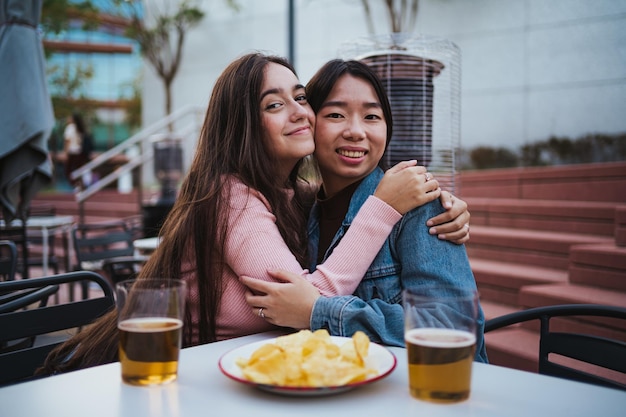 Dwie przyjaciółki przytulające się patrząc w kamerę Piją piwo na świeżym powietrzu