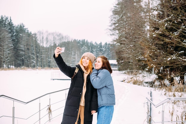 Dwie przyjaciółki zimą z telefonem robią selfie zimą