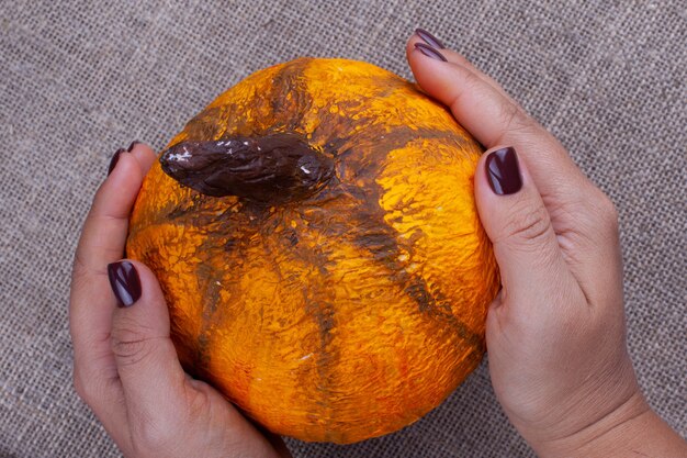 Dwie Ręce Trzymają Domowej Roboty Pomarańczową Dynię Z Papier-mache Na Halloween Na Płótnie, Widok Z Góry