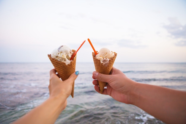 Dwie ręce trzymając smaczne lody na plaży latem.