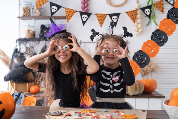 Dwie różne dziewczyny w stroju wiedźmy, bawiące się w domu w kuchni, świętujące Halloween.