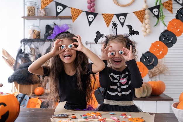 Dwie różne dziewczyny w stroju wiedźmy, bawiące się w domu w kuchni, świętujące Halloween.