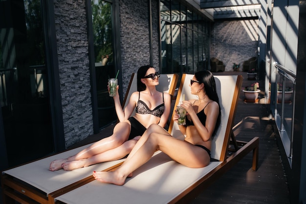 Dwie seksowne dziewczyny piją koktajle na basenie