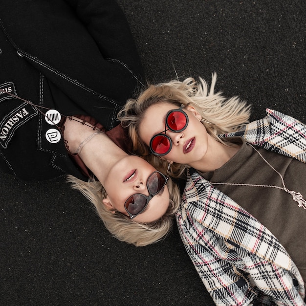 Zdjęcie dwie seksowne urocze lesbijki w modnym stroju na co dzień w modnych stylowych okularach odpoczywających na drodze na zewnątrz