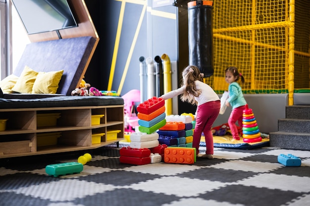 Dwie siostry bawiące się w centrum zabaw dla dzieci podczas budowania z kolorowych plastikowych klocków