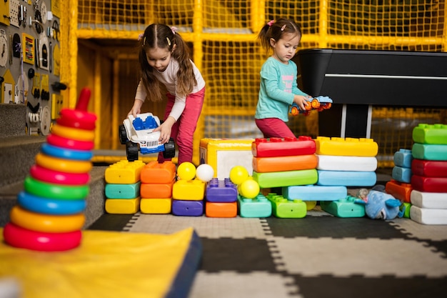 Dwie siostry bawiące się w centrum zabaw dla dzieci podczas budowania z kolorowych plastikowych klocków