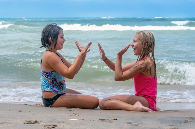 Zdjęcie dwie siostry grają w grę ręczną, siedząc na słonecznej plaży w michigan w usa.