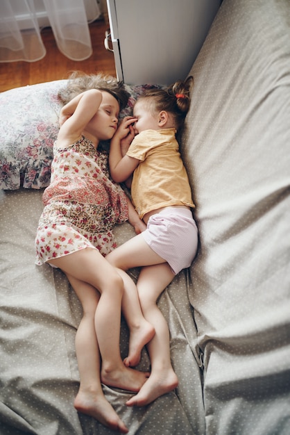Dwie siostry leżą obok siebie na łóżku i obejmują się