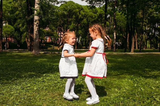 Dwie siostry skaczą, trzymając się za ręce, śmiejąc się i ciesząc się aktywnymi grami na świeżym powietrzu dla dzieci